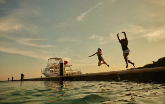 two women jump off a dock into the sea in Curacao