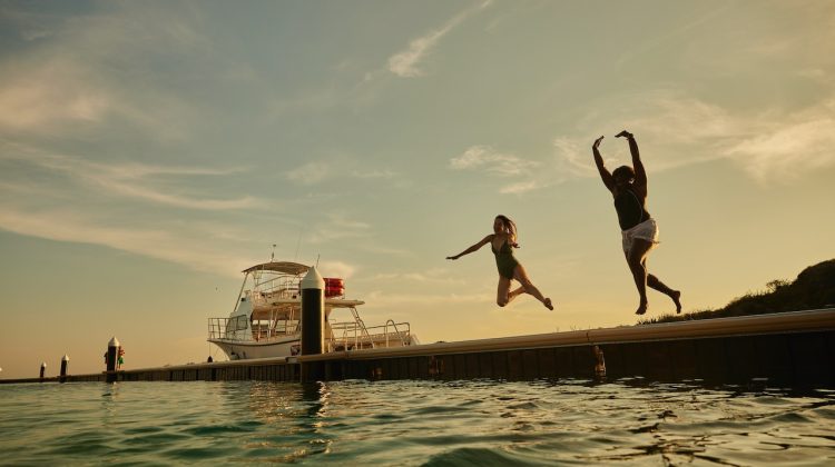 two women jump off a dock into the sea in Curacao