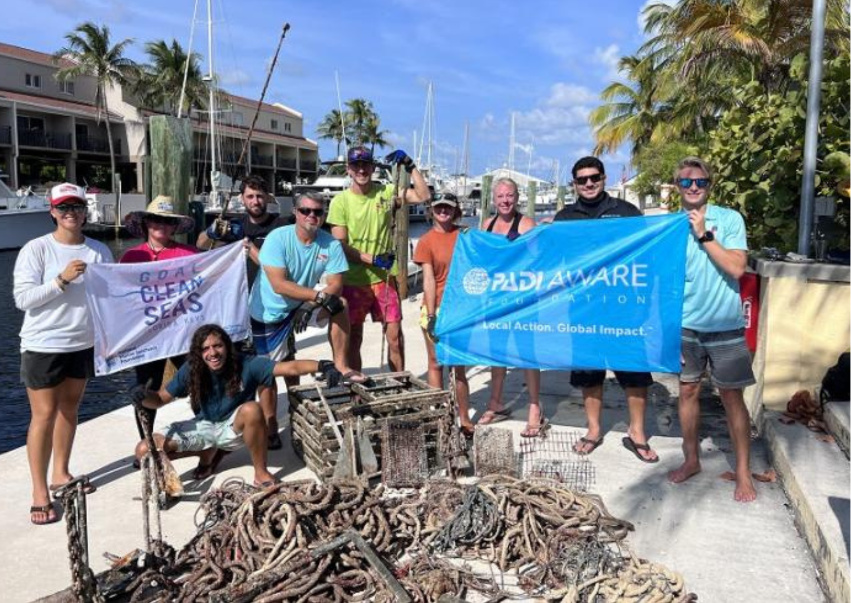 A group of people hold PADI AWARE signs up in front of a pile of marine debris that was recently removed from the ocean
