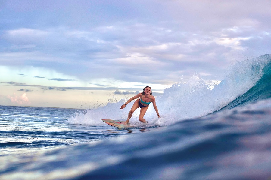 A woman surfs a wave at sunset in Moorea