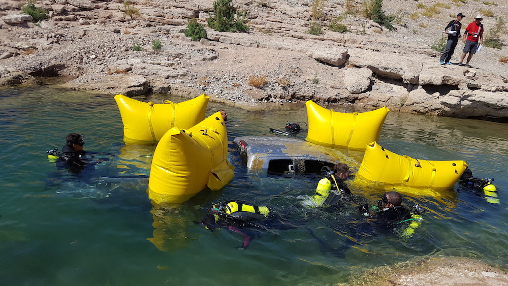 A group of divers use buoy bags to bring a pick up truck to the surface of a quarry