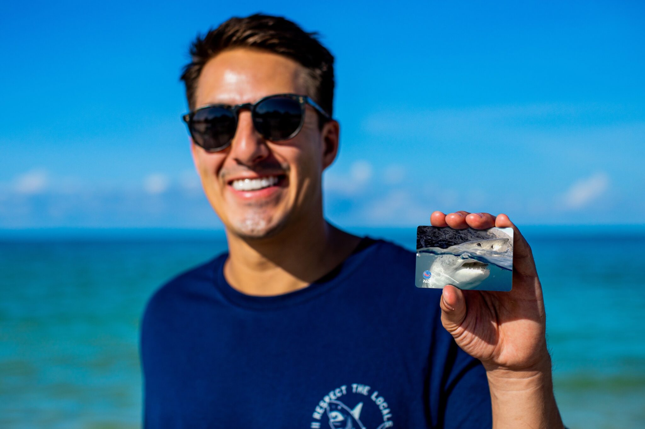 A man holds up a PADI certification card showing a great white shark