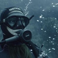 A woman diver sits serenely on the sea floor.
