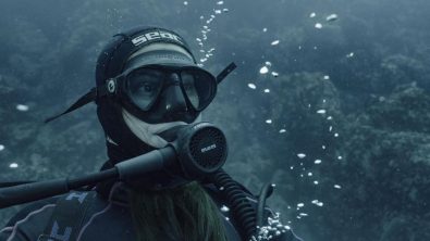 A woman diver sits serenely on the sea floor.