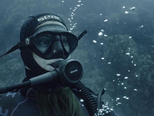 A woman diver sits serenely on the sea floor.