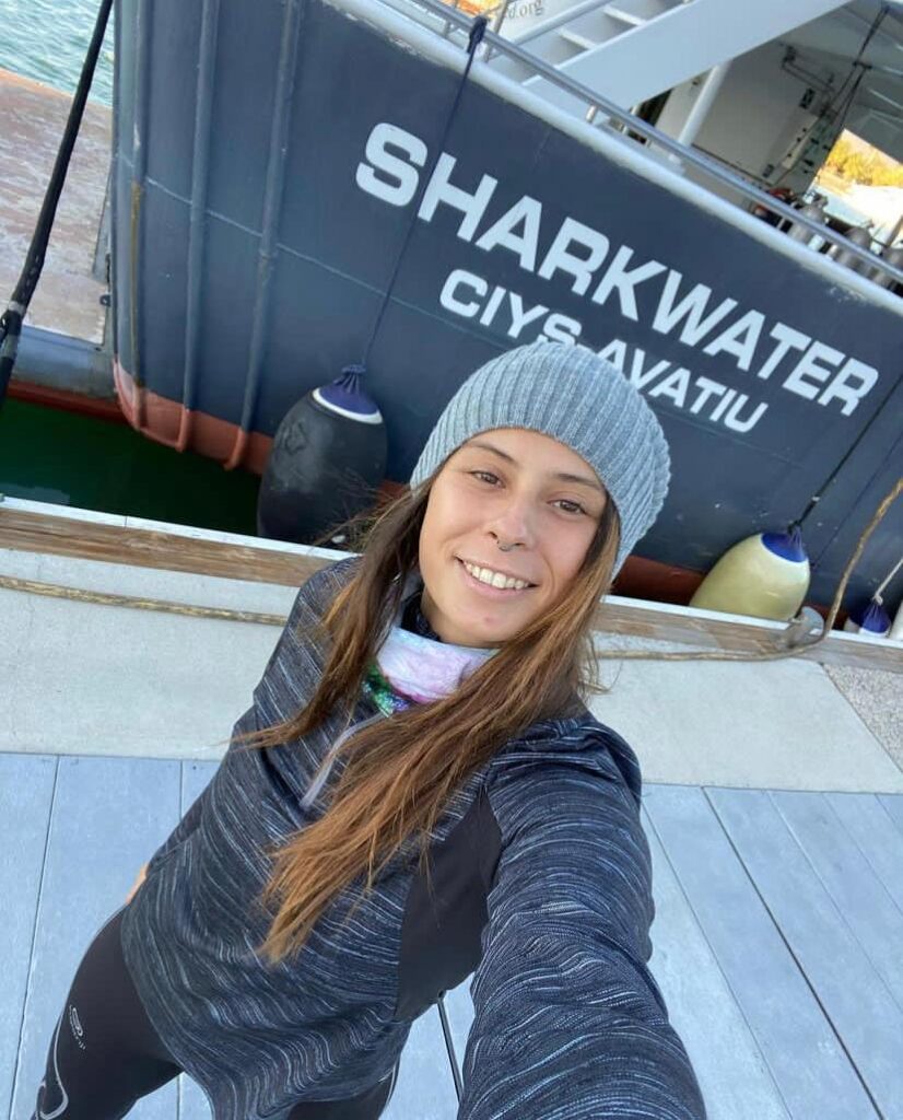 A woman takes a selfie in front of the vessel Sharkwater