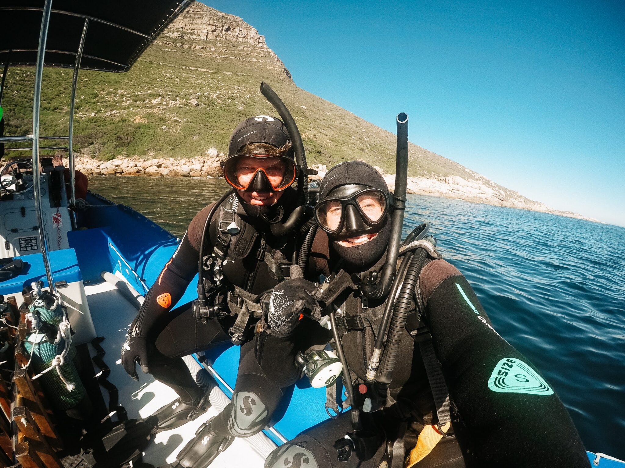 two divers sit on the side of a boat, getting ready for a scuba dive