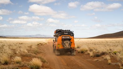An orange land rover drives across an African plane