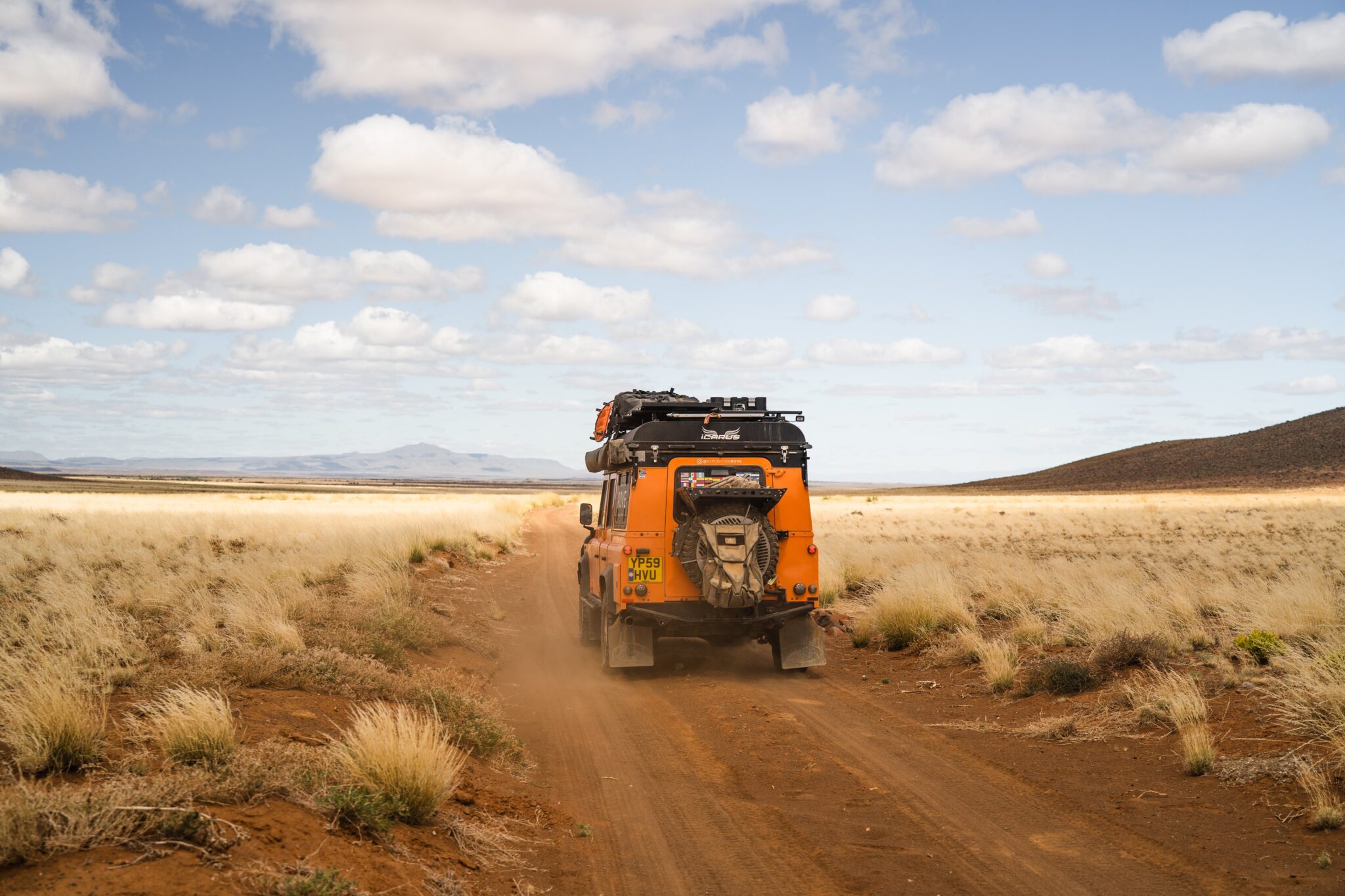 An orange land rover drives across an African plane