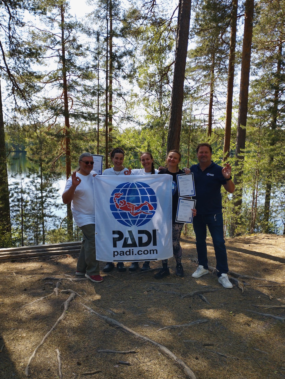 A group of PADI divers hold up the PADI flag in a forest in Finland