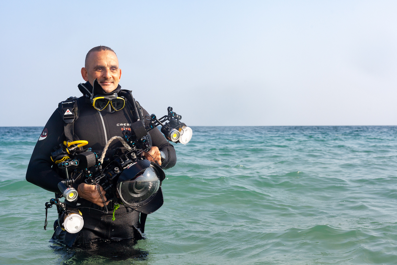 Zaki stands in the water holding an underwater camera