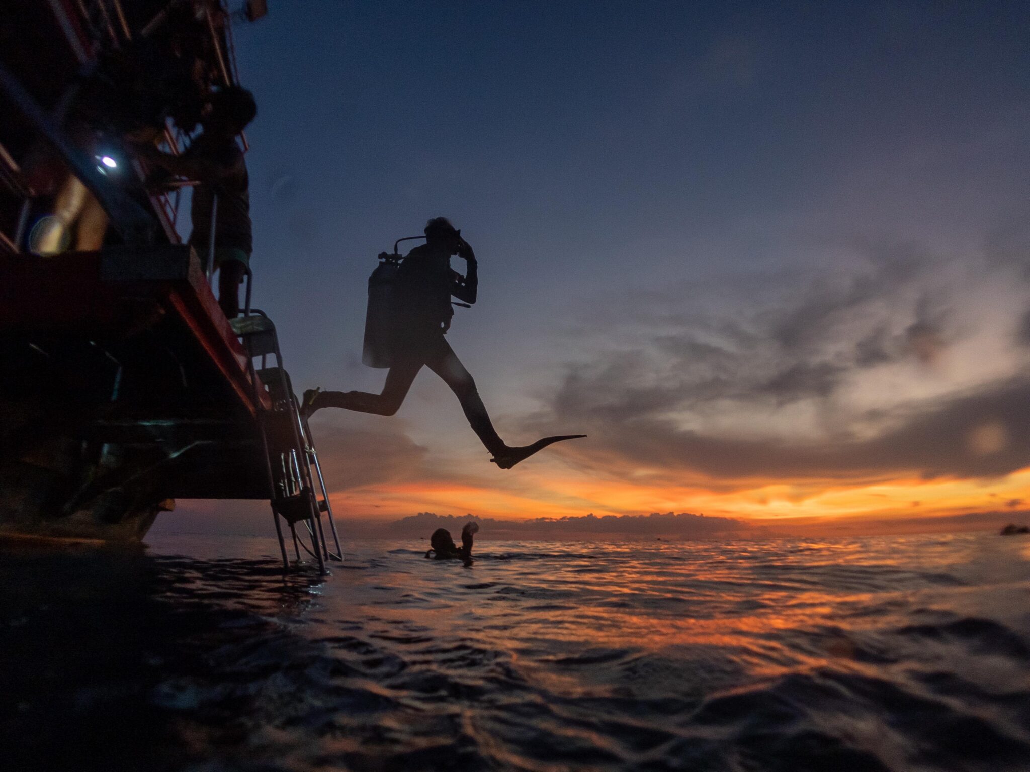 diver jumping off boat into the ocean at night