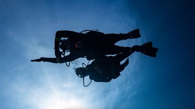 two divers in silhouette navigating underwater