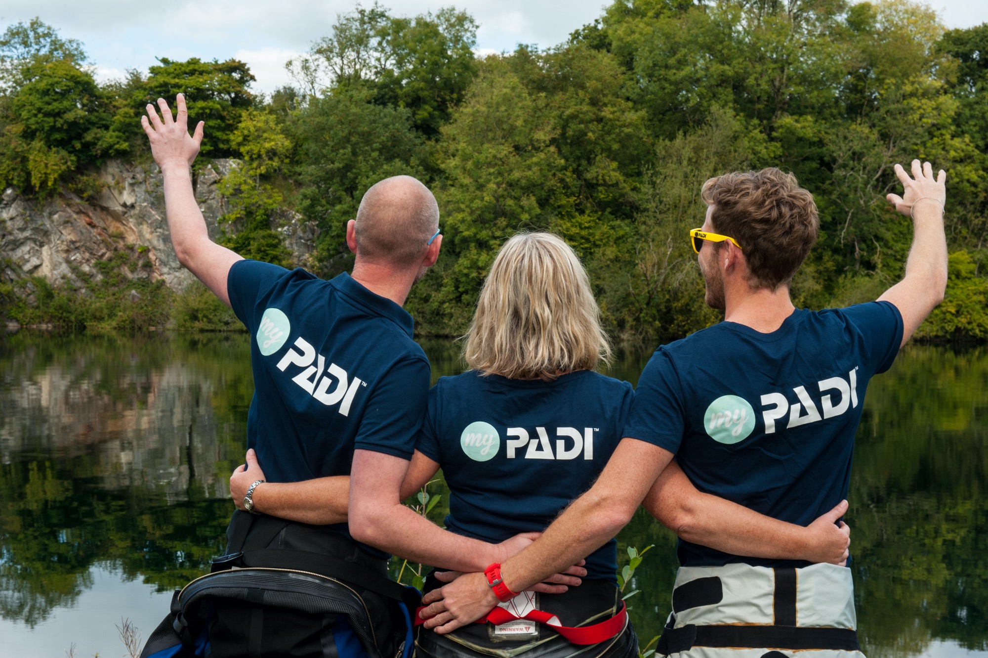 Three scuba diver friends standing next to an inland dive site, celebrating and cheering as they learn to dive in the UK