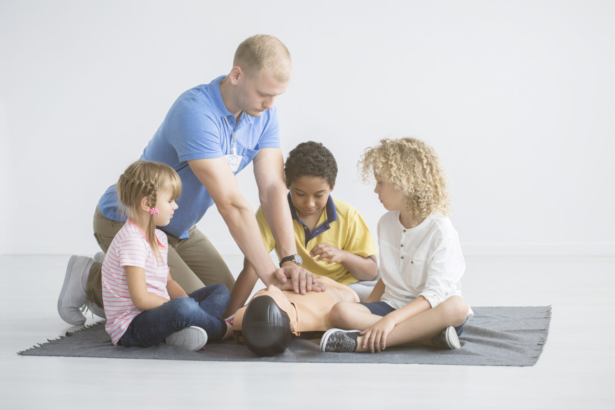 kids learn how to do cpr from an adult and a dummy