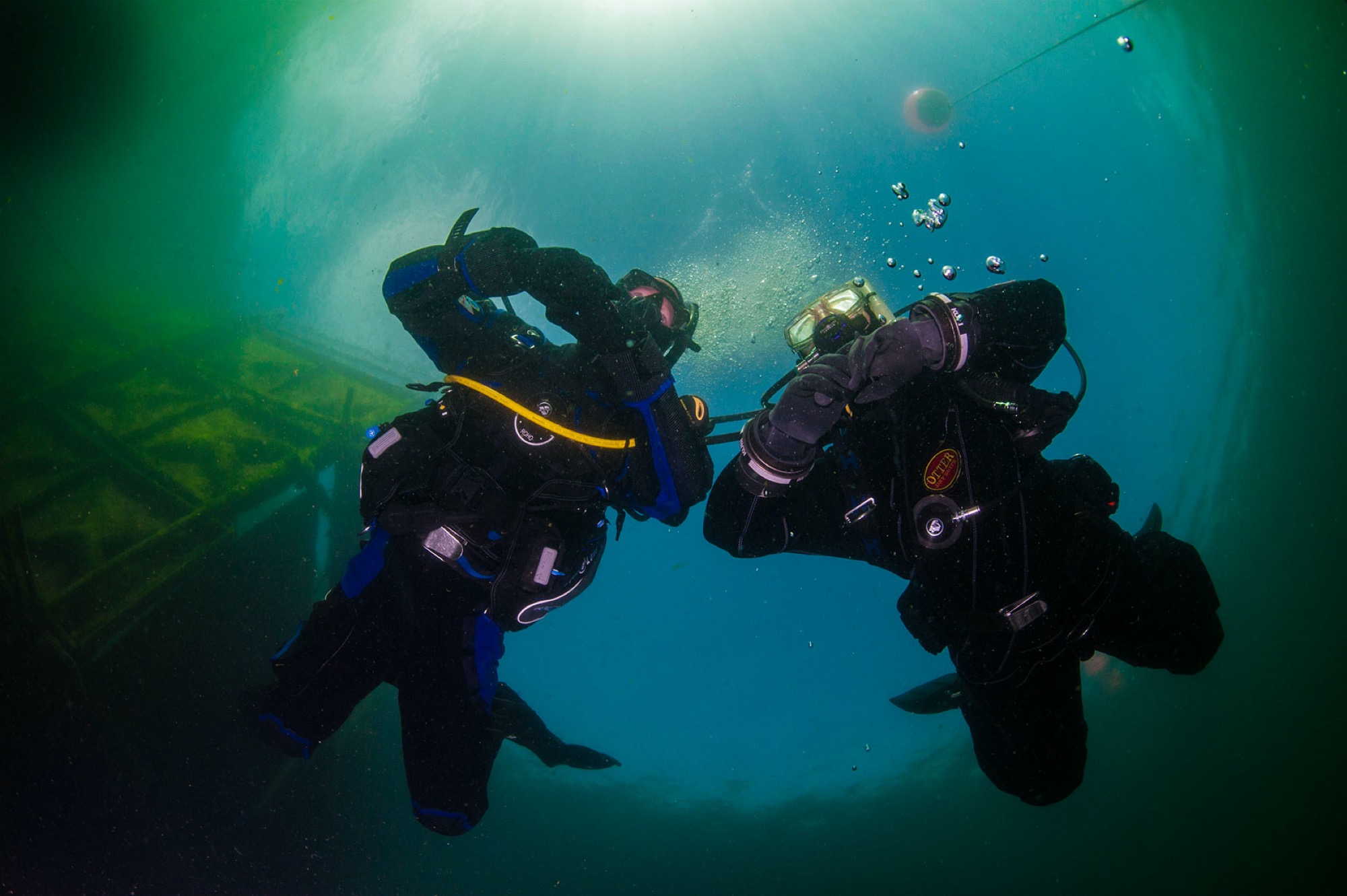 Two scuba divers in drysuits are ascending safely and slowly to the surface as they know rapid ascents can cause diving bends