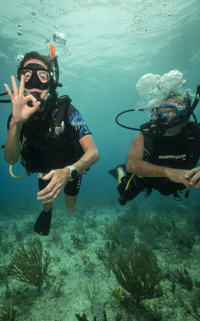 An adaptive diver gives the "okay" sign on her certification dive. Her instructor floats near her.