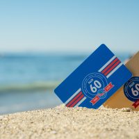 Two certification cards showing PADI's 60th anniversary logo propped up on the sand