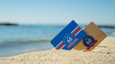 Two certification cards showing PADI's 60th anniversary logo propped up on the sand