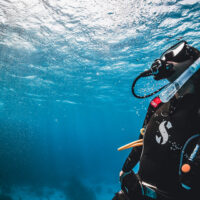 a scuba diver looks up towards the surface in a a clear blue sea
