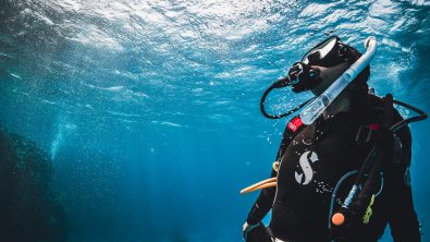 a scuba diver looks up towards the surface in a a clear blue sea