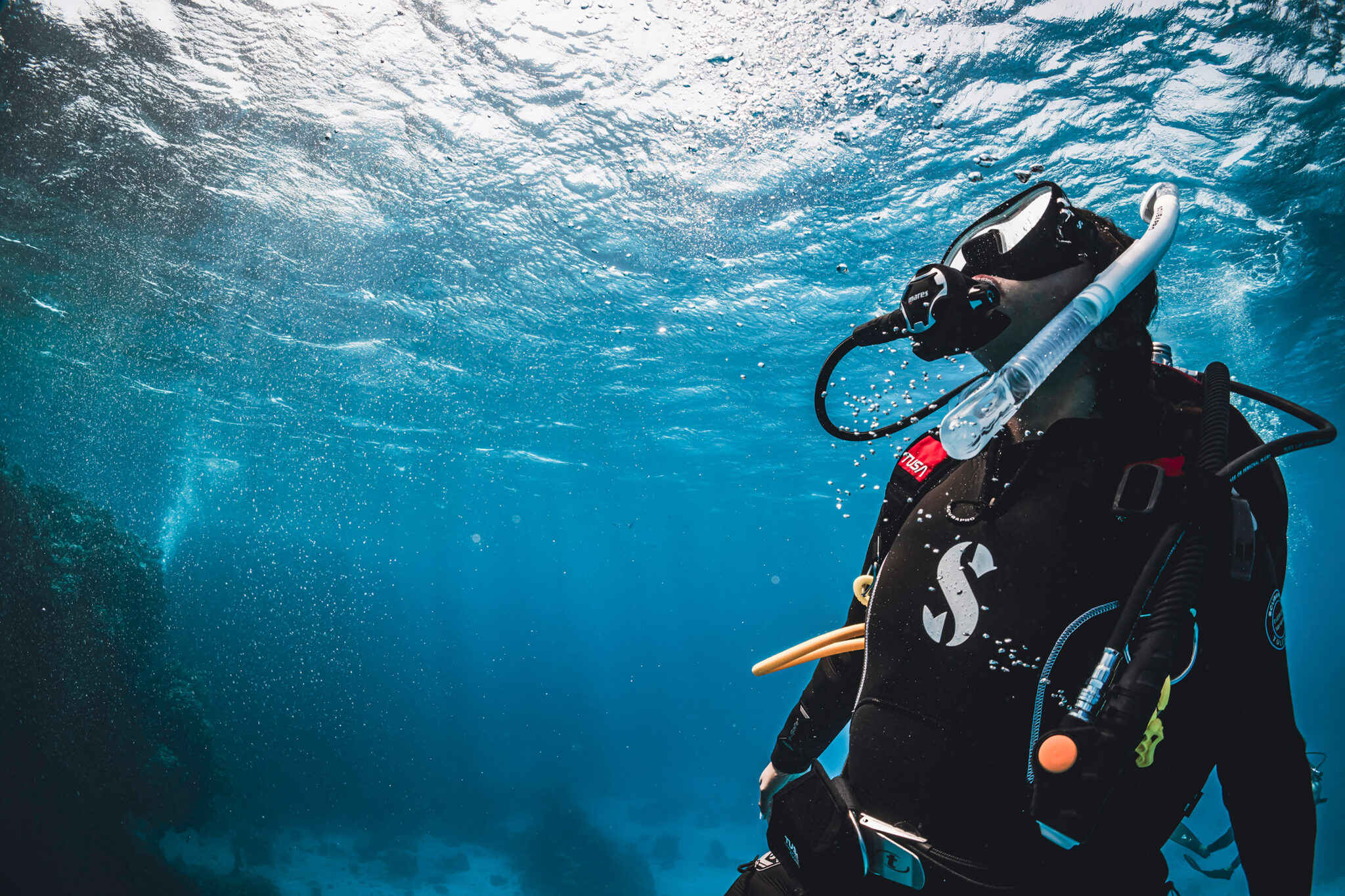 a scuba diver looks up towards the surface in a a clear blue sea