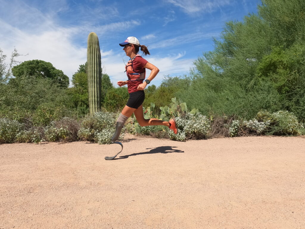 A runner with a prosthetic leg runs on an unpaved path linked with desert vegetation.