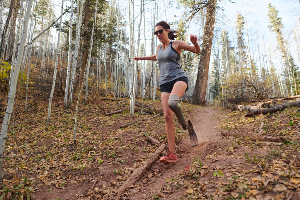 A runner with a prosthetic leg runs down a trail in a wooded area.