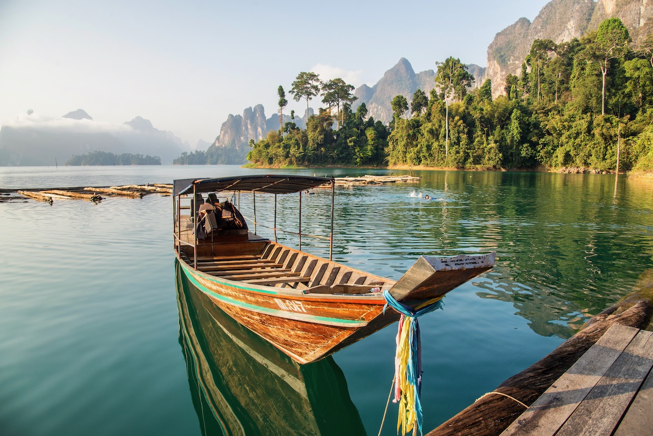 long tail boat on floating bamboo raft with beautiful lake and mountain background in the morning at ratchaprapa dam , khao sok national park in surat thani southern of thailand