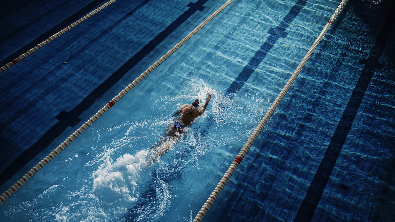 Female Swimmer Racing in Swimming Pool. Professional Athlete Overcoming Stress and Hardships in Dark Dramatic Pool, Cinematic Lap Lane Light Showing the Good Way. Aerial Shot