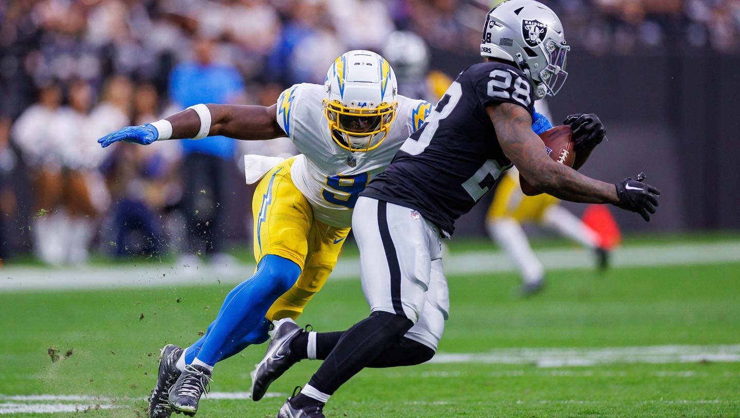 A football player in white, yellow and blue  prepares to tackle another player about to catch the ball.