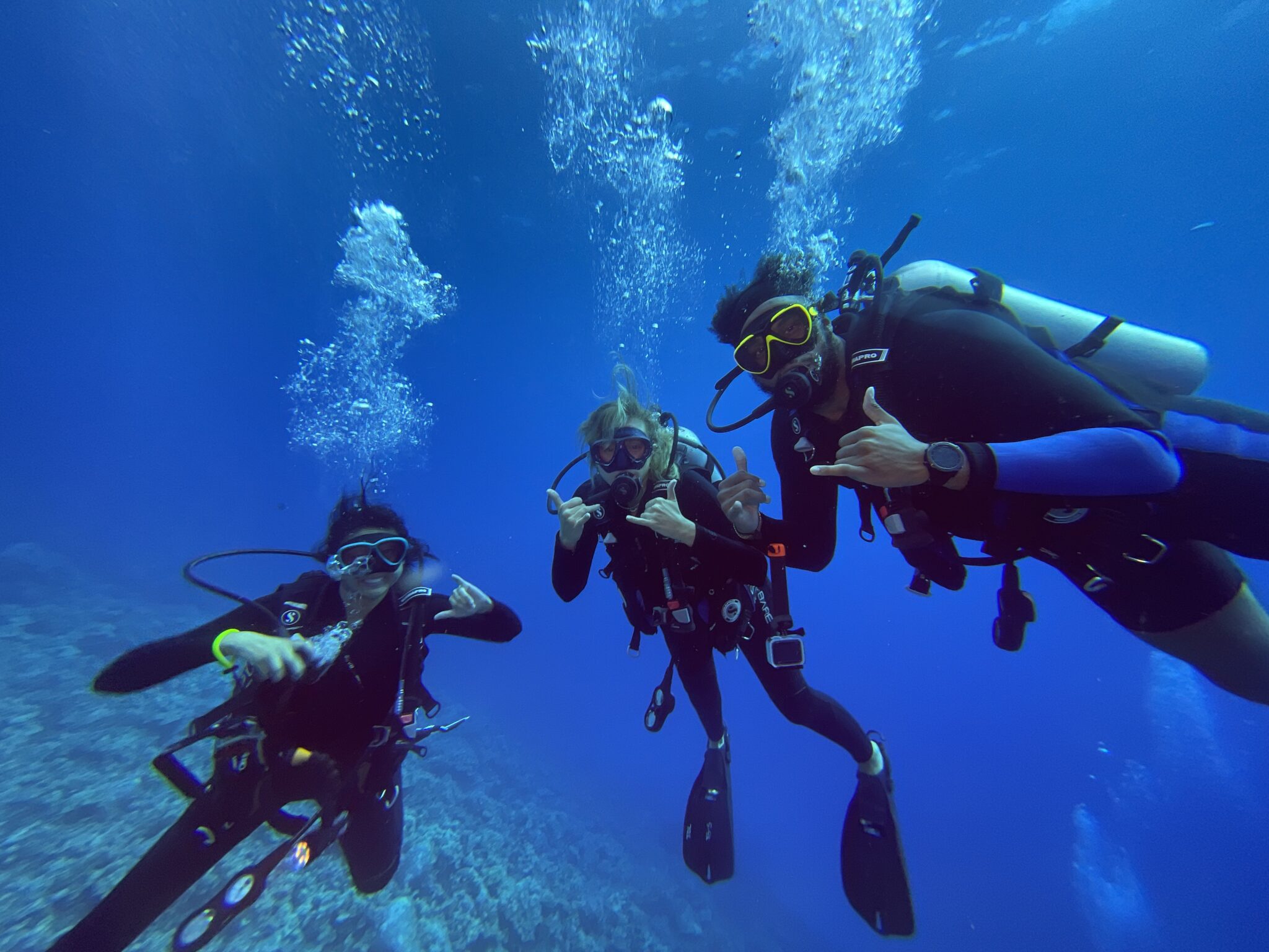 Three divers pose for a photo underwater with the hang ten sign.