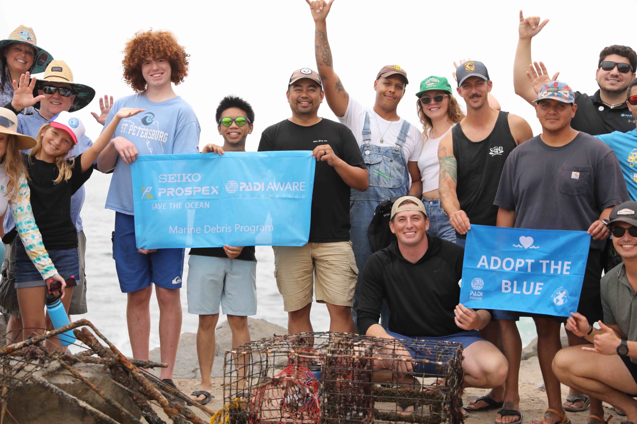 A group of people pose on the beach in front of marine debris while holding up adopt the blue and padi aware signs