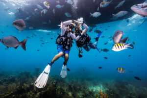 divers underwater in Belize make a heart shape with their arms