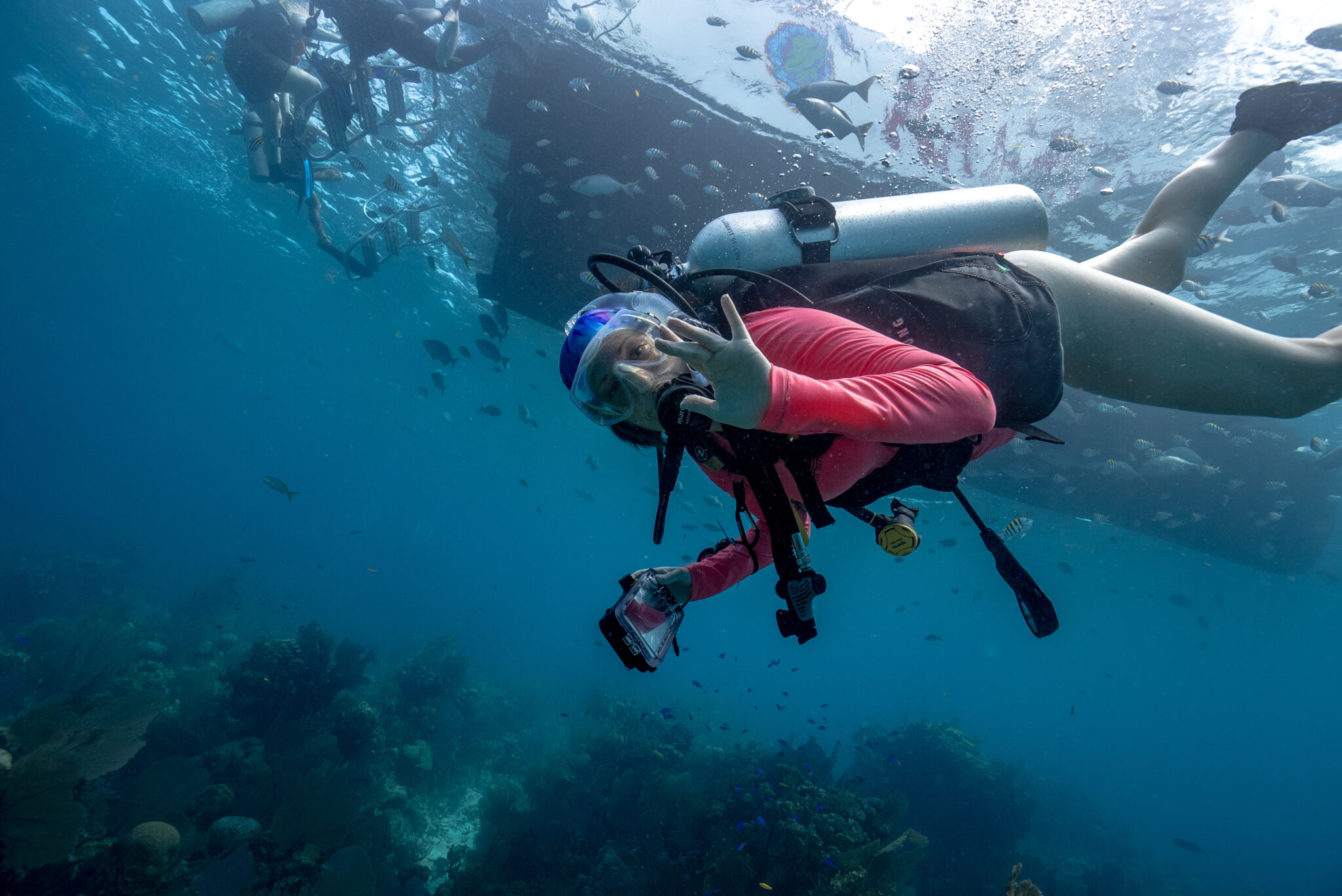 A female scuba diver waves to the camera underwater in Belize while on a PADI Club trip