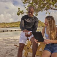 two divers at the beach, one holding a mobile phone and another holding a tablet