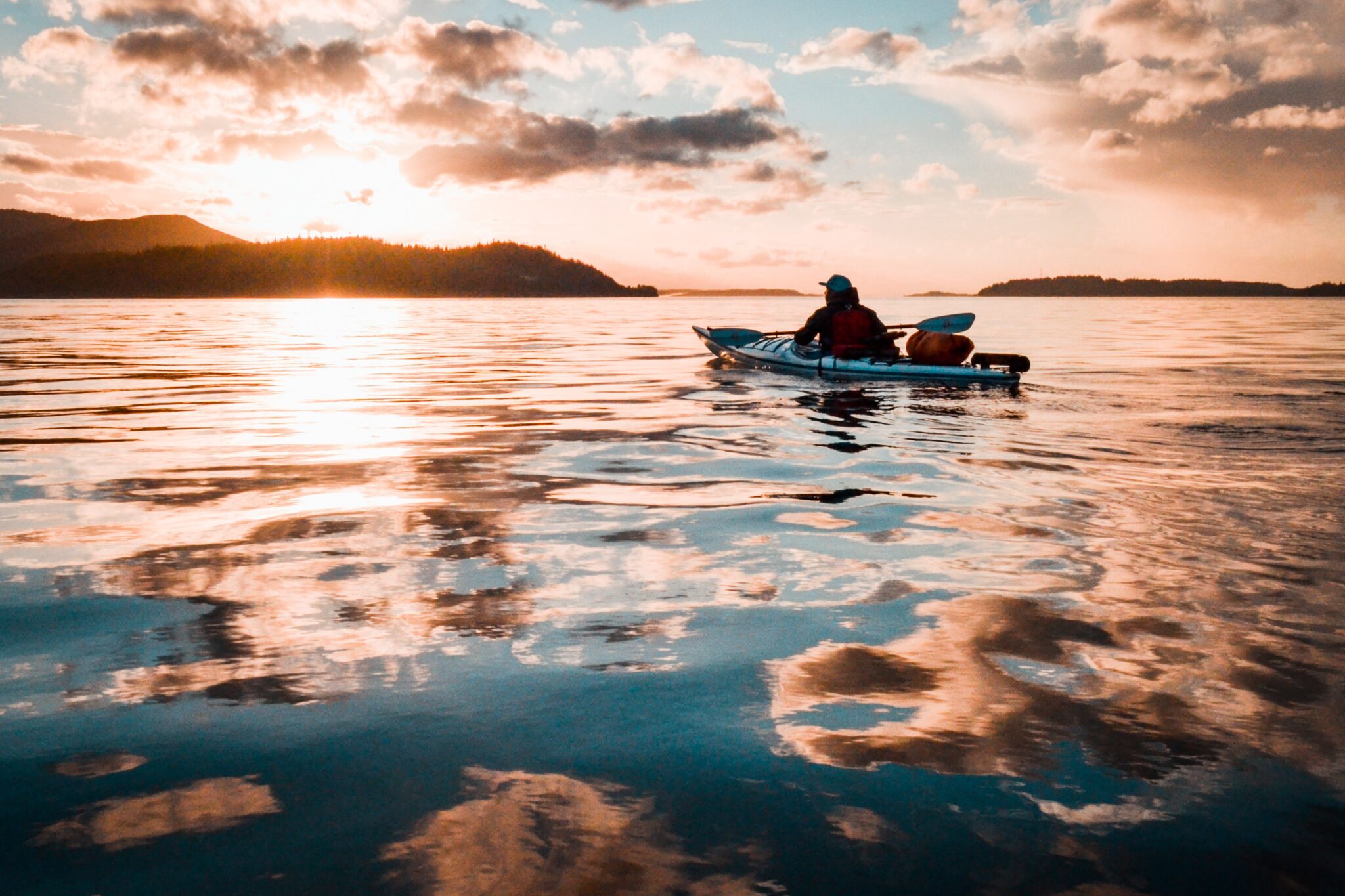 A man kayaks into the sunset on glassy water