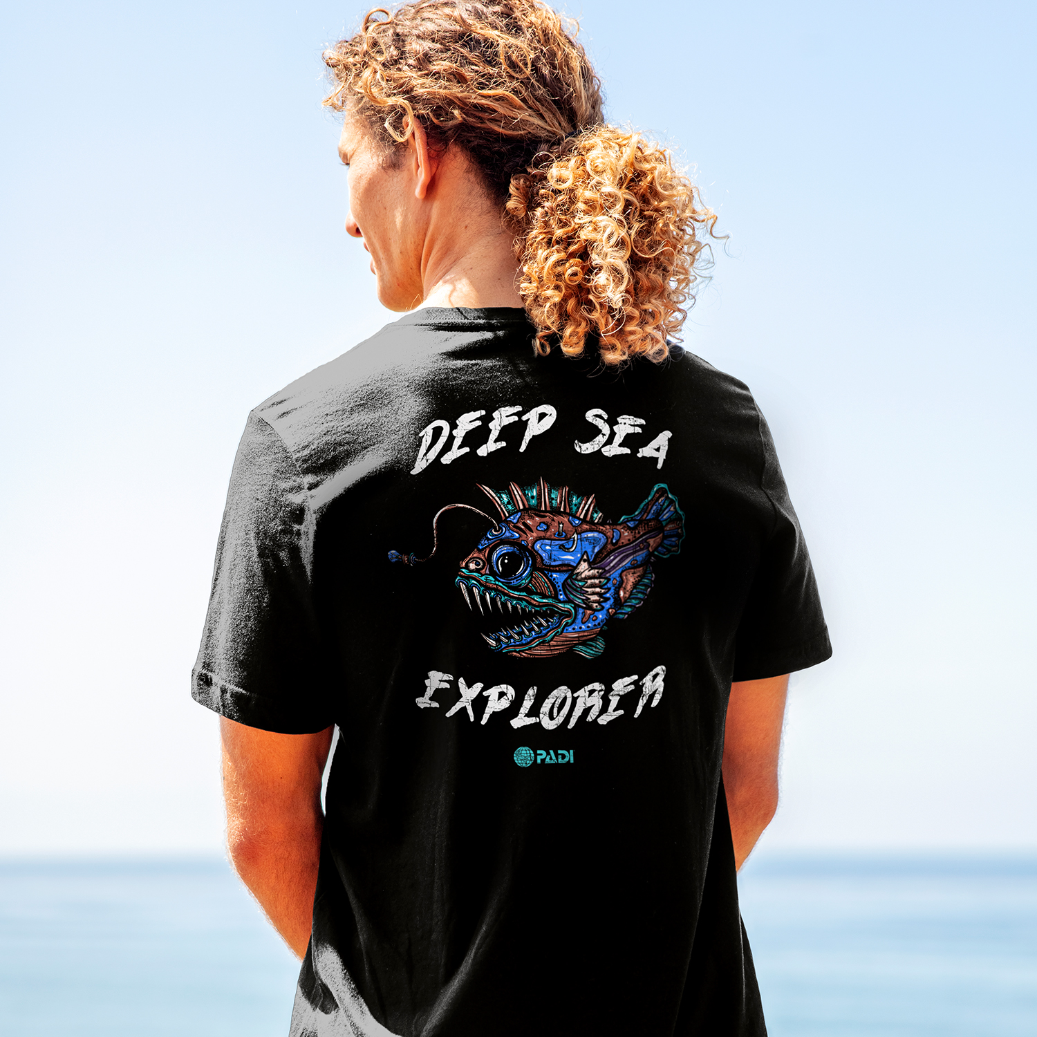 A man wears a sea creature tshirt showing a deep sea fish with the PADI logo