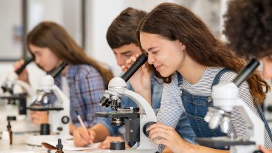 Three students look into microscopes in a science lab classroom