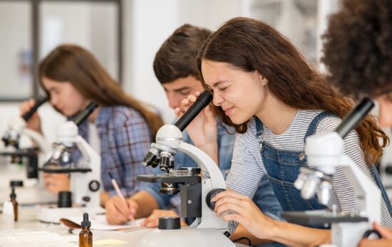 Three students look into microscopes in a science lab classroom