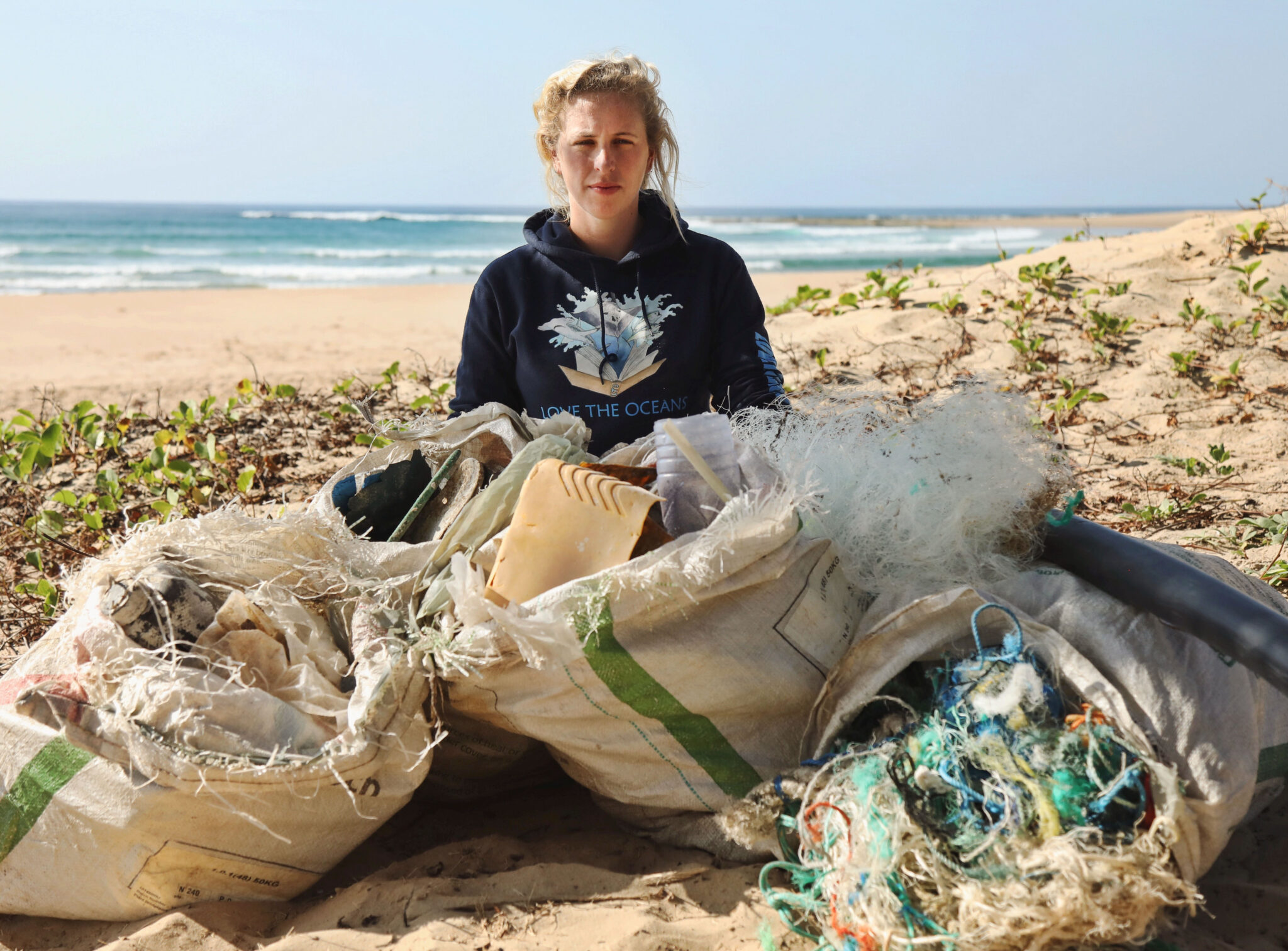 Francesca Trotman sits on a beach with rubbish she has collected
