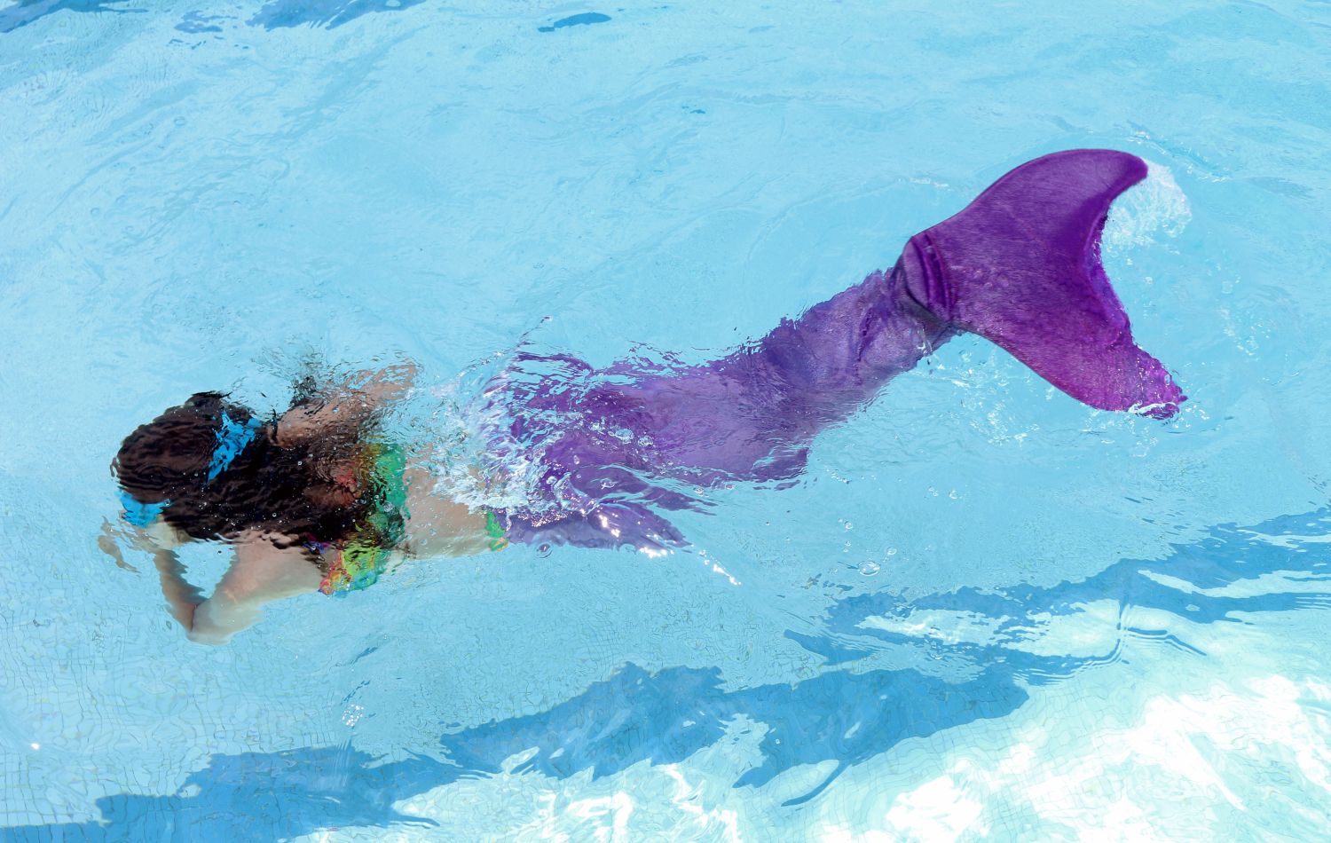 Child wearing a mermaid tail in the pool.