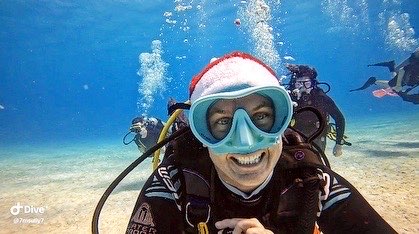 Female diver smiling at the camera underwater with a santa hat