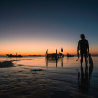a diver exits the water onto the shore at sunset