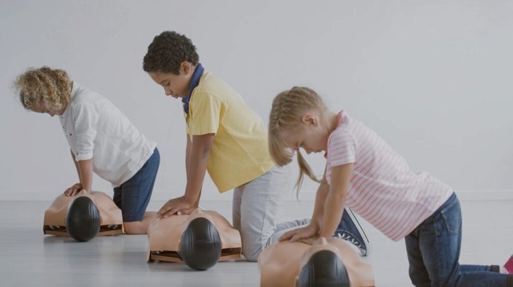 three children learn CPR using dummies