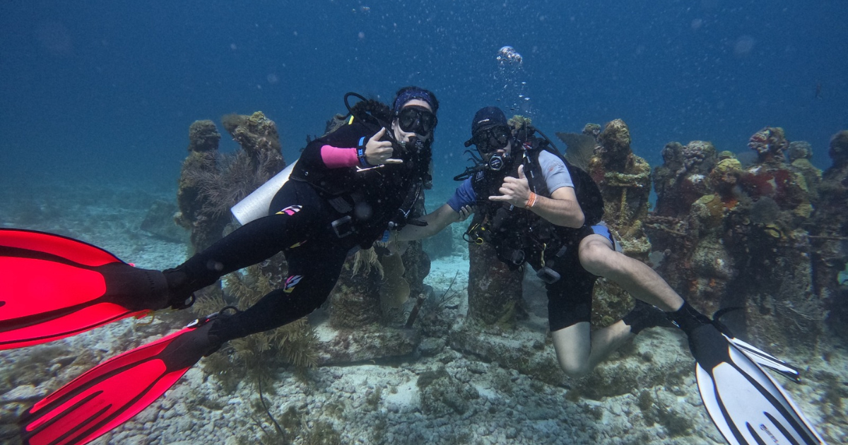 Two divers pose for the camera next to underwater statues