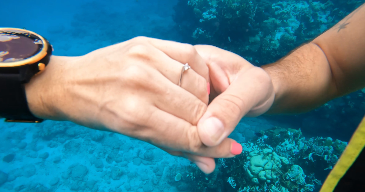 A couple's hands underwater. The woman is wearing a ring.