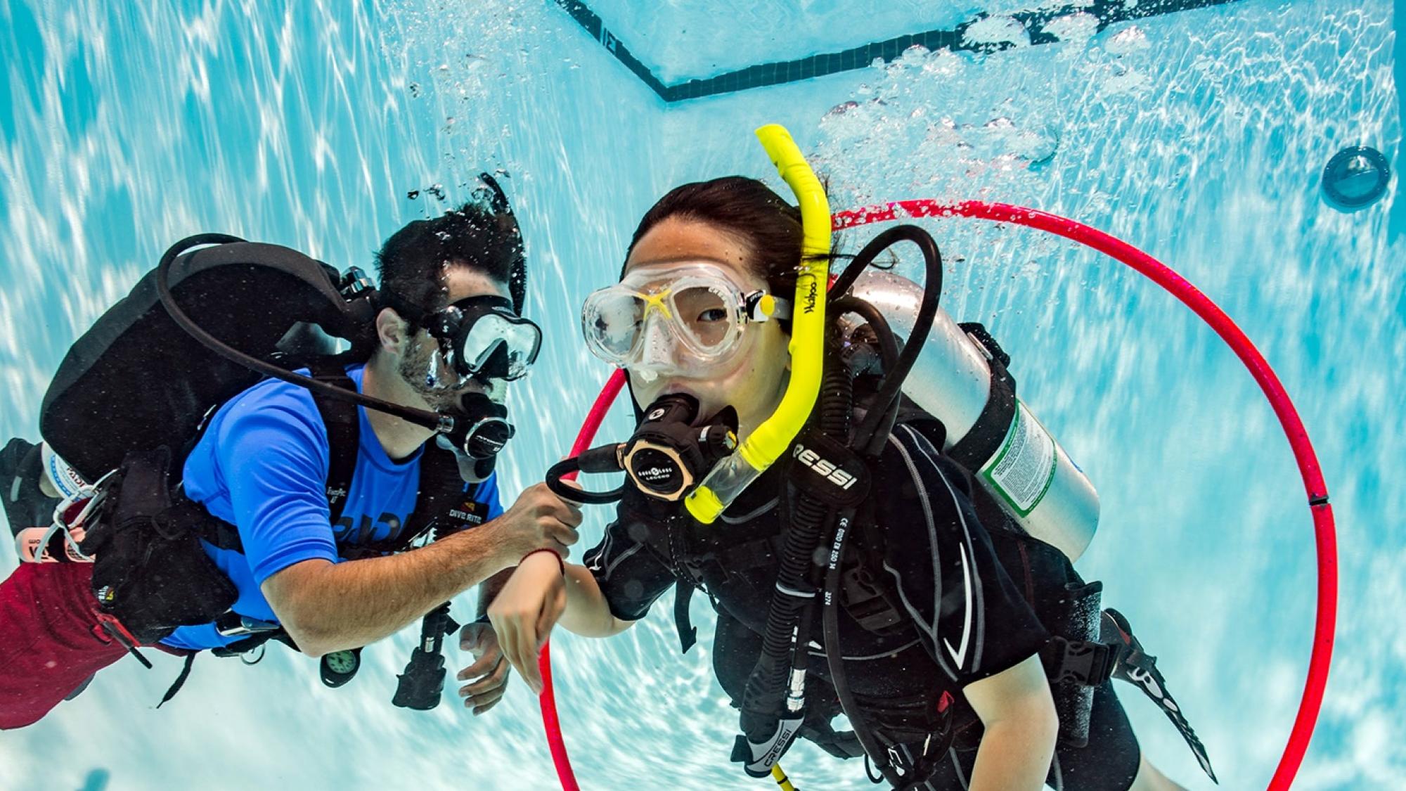 A PADI Instructor helps a PADI Seal Team participant swim through an underwater hula hoop as part of a buoyancy AquaMission