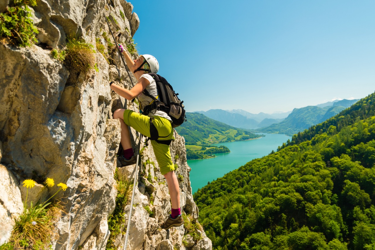 Beautiful young girl climbing Drachenwand via ferrata high above scenic Mondsee lake, Austria