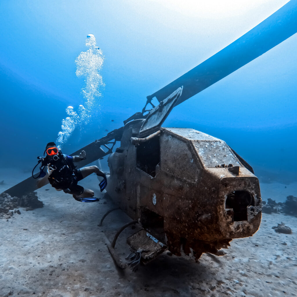A scuba diver explores a helicopter while his friend records him using a gopro